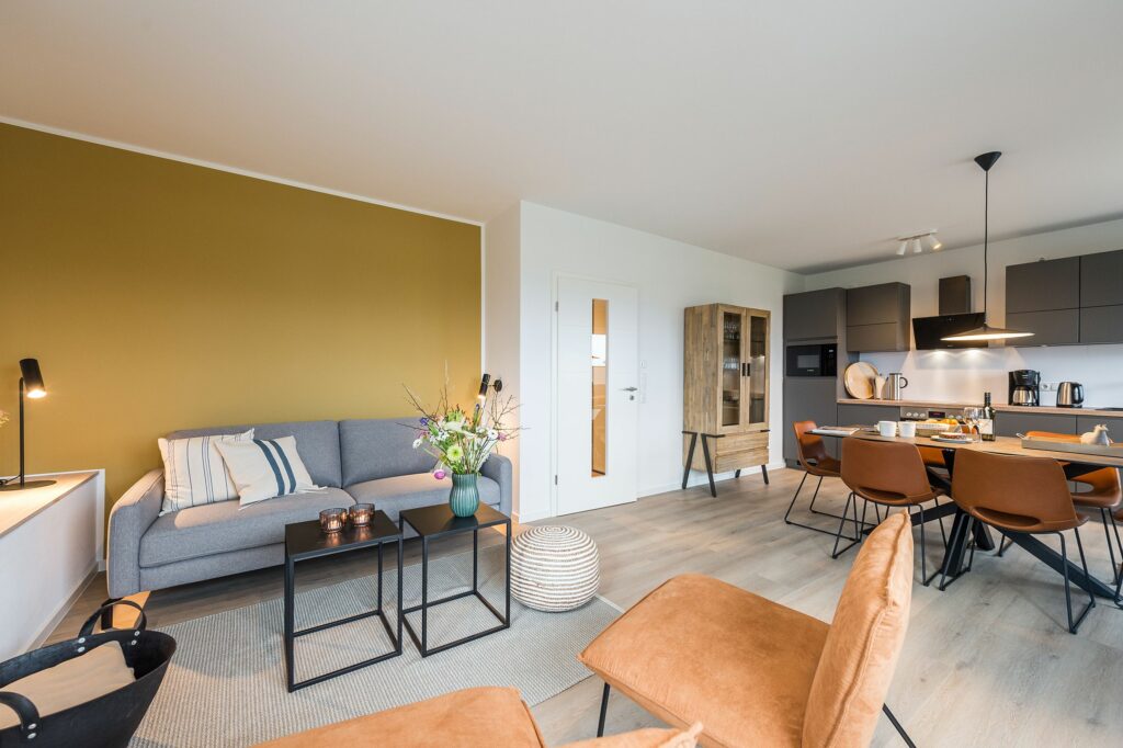 Offene Wohnküche mit gelber Wand und großem Esstisch für sechs Personen in Ferienwohnung Grömitz