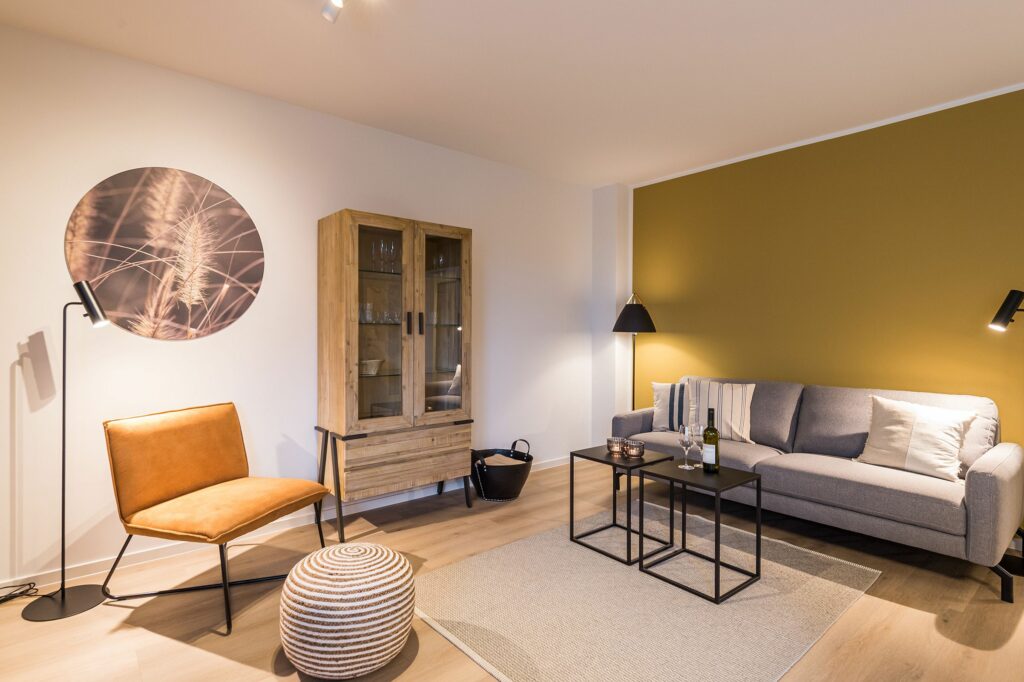 Wohnzimmer mit gelber Wand, Vitrine und grauem Sofa in Ferienwohnung Grömitz