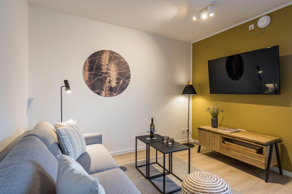 Wohnzimmer mit gelber Wand, Fernseher und grauem Sofa in Ferienwohnung Grömitz