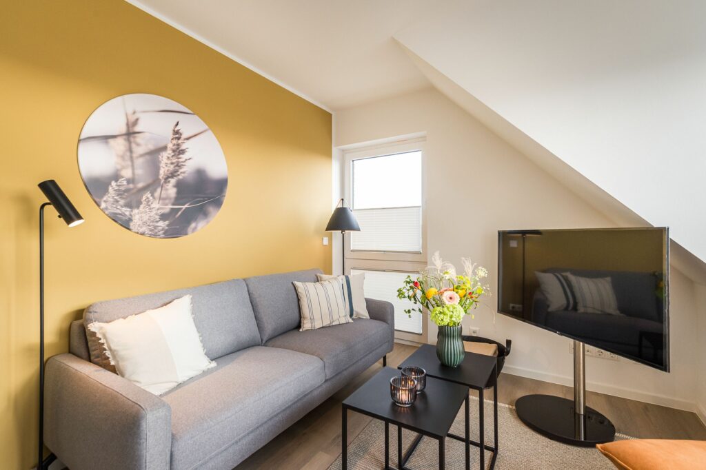 Wohnzimmer mit gelb gestrichener Wand und hellgrauem Sofa in Ferienwohnung Grömitz