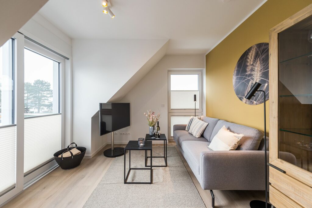 Dachgeschoss Wohnzimmer mit gelber Wand und Fernseher in Ferienwohnung Grömitz