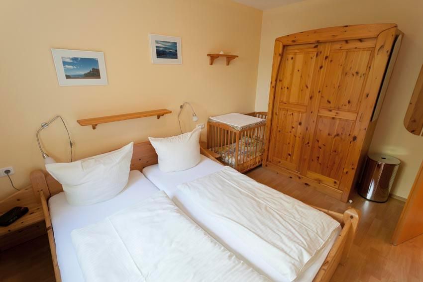 Ein Schlafzimmer mit einem Doppelbett und einem Beistellbett für Kleinkinder in einer Ferienwohnung an der Ostsee.