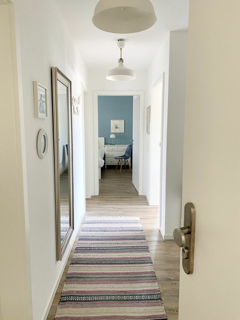 Flur mit großem Spiegel und Teppich, Blick in ein blau gestrichenes Schlafzimmer im Ferienhaus Grömitz