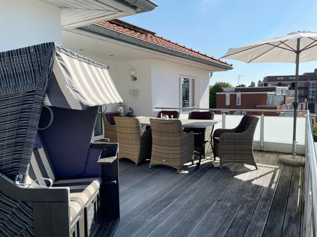 Balkon mit Flechtstuhl-Sitzgruppe und Sonnenschirm sowie einem Strandkorb im Ferienhaus Grömitz