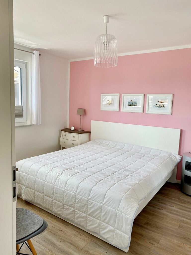 Schlafzimmer mit rosa gestrichener Wand und Doppelbett im Ferienhaus Grömitz
