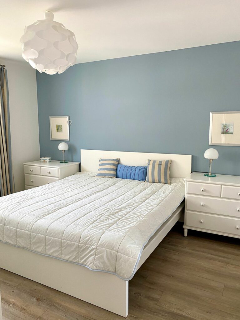 Schlafzimmer mit blau gestrichener Wand und Doppelbett im Ferienhaus Grömitz